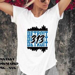 May include: White t-shirt featuring a blue and black graphic design. The design includes the text "DETROIT 313 DETROIT" in a stacked format, with a cityscape silhouette above and below the text. The words "INSTANT DOWNLOAD PNG SVG" are at the bottom.