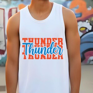 May include: White tank top with the word "Thunder" in orange block letters, with a blue cursive "Thunder" overlay. The tank top is sleeveless and has a crew neck.