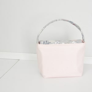 Pu&ograve; includere: Una borsa tote in tessuto rosa con pois bianchi e una fodera in tessuto floreale grigio. La borsa ha un'unica maniglia.