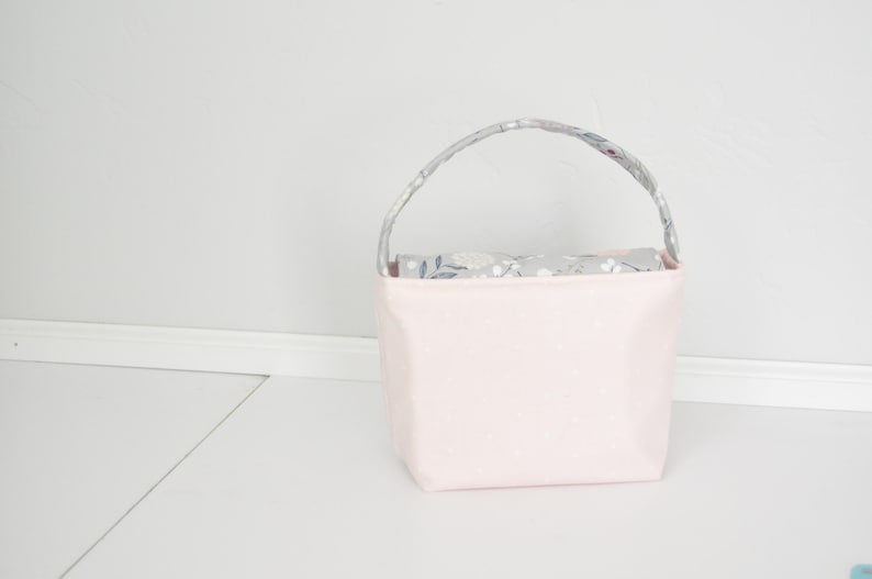 Pu&ograve; includere: Una borsa tote in tessuto rosa con pois bianchi e una fodera in tessuto floreale grigio. La borsa ha un'unica maniglia.