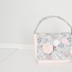 Könnte beinhalten: Eine kleine graue und rosafarbene Stofftasche mit Blumendruck und einem rosafarbenen Stoffblumen-Akzent.