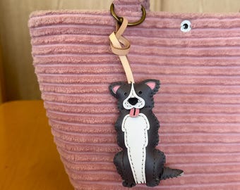 May include: A pink corduroy tote bag with a matching handle and a decorative dog-shaped charm. The charm is black, white, and pink, with a tongue sticking out. The bag has a metal ring and a leather strap.