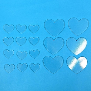 May include: Clear acrylic heart shapes in various sizes, arranged on a blue background. The hearts range from small to large, with smooth edges. Ideal for crafting or decorative projects.