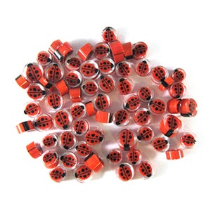 Puede incluir: Un gran grupo de cuentas de vidrio de color rojo y negro con forma de mariquita. Las cuentas son transparentes y tienen un diseño de mariquita negra.