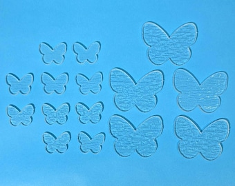 May include: A collection of clear acrylic butterfly shapes in various sizes, arranged on a solid blue background. The butterflies have a textured appearance, and the arrangement suggests a craft or decorative theme.