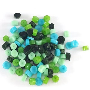 May include: A collection of small, round, and cylindrical beads in shades of green, blue, and black. The beads are made of glass or plastic and have a smooth, glossy finish.