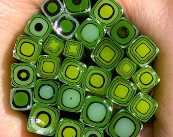 May include: A bundle of square glass rods featuring concentric green and black patterns. Each rod displays a unique arrangement of lime, forest, and pale green squares with thin black outlines, creating a geometric, layered effect across the ends.
