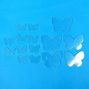 May include: Clear acrylic butterfly cutouts of various sizes are arranged on a bright blue background. The butterflies are transparent and have a simple, symmetrical design. The arrangement includes several small and larger butterflies.