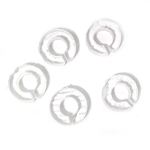 May include: Six white plastic rings, each with a small opening in the center. The rings are arranged in a circle on a white background.