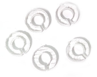 Puede incluir: Seis anillos de plástico blanco, cada uno con una pequeña abertura en el centro. Los anillos están dispuestos en círculo sobre un fondo blanco.