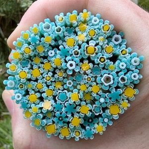 Peut inclure: Gros plan sur un ensemble de baguettes de verre colorées avec un motif floral. Les baguettes sont principalement turquoise et jaunes, avec des accents blancs et bleu foncé. Les extrémités des baguettes sont visibles, révélant les motifs floraux complexes.