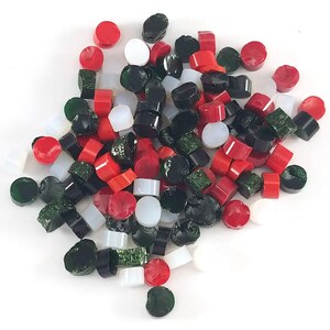 May include: A collection of small, colorful glass pieces in various shapes. The assortment includes red, green, black, and white pieces, some cylindrical and others rounded. The pieces are scattered on a white surface.