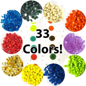 Op de afbeelding: Assortiment van 33 kleuren kleine plastic korrels. De korrels zijn gerangschikt in een cirkel met een witte achtergrond.