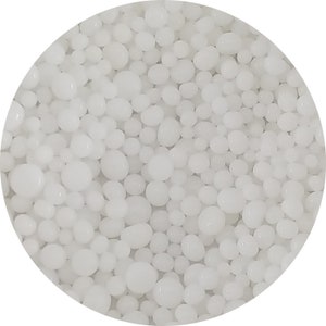 May include: A close-up view of a pile of white, round, and slightly irregular-shaped granules. The granules are all about the same size and are tightly packed together.