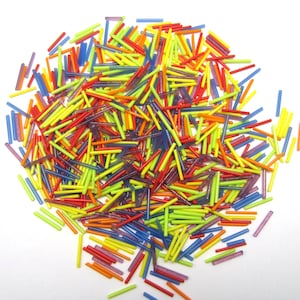Peut inclure: Un grand tas de tiges de verre colorées dans des tons de jaune, rouge, orange, bleu et violet. Les tiges sont disposées de manière aléatoire et ont toutes à peu près la même taille.