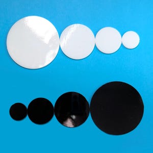 May include: A set of six round, flat, adhesive-backed circles in two sizes and two colors. There are three white circles and three black circles. The circles are arranged in two rows, with the larger circles in the front and the smaller circles in the back.