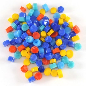 May include: A collection of small, round glass tiles in blue, yellow, and red colors. The tiles are scattered on a white surface.