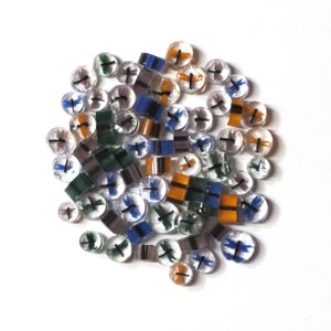 Puede incluir: Una colección de cuentas de vidrio con diseños de libélulas en tonos de azul, verde, naranja y negro. Las cuentas son transparentes y tienen una apariencia translúcida.