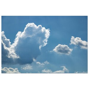 May include: A bright blue sky filled with large, fluffy white cumulus clouds. The clouds exhibit varying shades of white and soft gray, with sunlight illuminating their edges, creating a high-contrast appearance against the clear blue atmosphere.