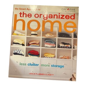 May include: A book cover titled "the organized home" with the text "less clutter more storage". The cover features a grid of shelves with folded clothes, hats, and shoes. The book is by Leslie Plummer Clagett.