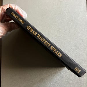 May include: A black hardcover book titled "Oprah Winfrey Speaks" by Janet Lowe. The title and author's name are in gold lettering. The Wiley logo is visible on the bottom right corner of the book.
