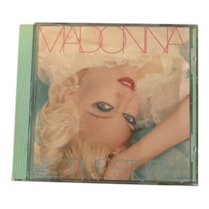 Op de afbeelding: CD-hoesje met de albumhoes van Madonna's "Like a Prayer". De cover toont een close-up van Madonna's gezicht, met blond haar en rode lippenstift. De albumtitel staat in een roze lettertype.