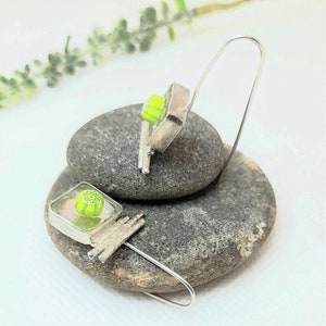 Pu&ograve; includere: Un paio di orecchini d'argento con quadrati di vetro verde e bianco. Gli orecchini sono appesi a un filo d'argento.