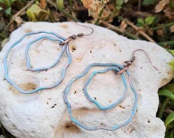 May include: A pair of turquoise blue copper wire earrings with a wavy, organic shape. The earrings are double-layered and have a rustic, handmade look.