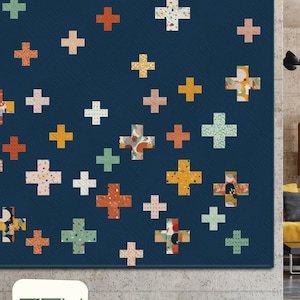 May include: A navy blue quilt with a repeating plus sign pattern in various colors, including orange, yellow, and green. The quilt features the text "PLUSES" and the "ZEN CHIC" logo.