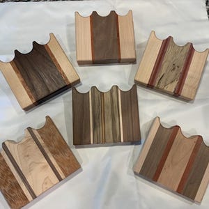 May include: Six wooden coasters with a wavy edge and a multi-colored wood grain pattern. The coasters are made of maple, walnut, and cherry wood.