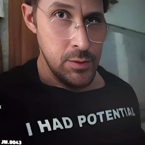 May include: A person wearing a black t-shirt with the white text "I HAD POTENTIAL". The person is wearing glasses with a thin, gold-coloured frame. The image has a slightly blurred quality.