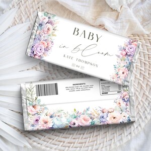 Könnte beinhalten: Zwei Schokoladenriegelverpackungen mit floralen Designs und dem Text "BABY in bloom". Die Verpackungen zeigen pastellfarbene Blumen in Rosa, Lila und Blau. Der Text enthält den Namen "KATE THOMPSON" und das Datum "SAT 04 OCT."