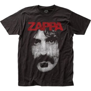 Puede incluir: Camiseta gris oscuro con una imagen en blanco y negro de un rostro masculino y la palabra "ZAPPA" en rojo. La camiseta tiene cuello redondo y mangas cortas. La imagen presenta a un hombre con bigote.