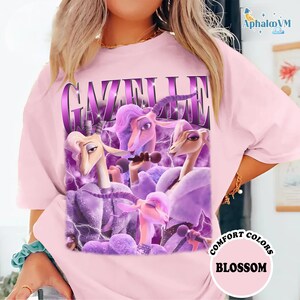A woman wearing a pink t-shirt with a graphic design featuring purple and pink cartoon animals, including a unicorn and a dragon, along with the text "Gazelle" and "Blossom".
