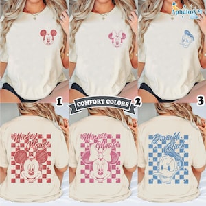 May include: Cream-colored t-shirts featuring Mickey Mouse, Minnie Mouse, and Donald Duck designs. The front of each shirt has a small character graphic, while the back displays a larger image with the character's name and a checkered background. The text "COMFORT COLORS" is also visible.