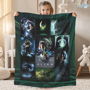 May include: A green and black Alien-themed blanket featuring a collage of images from the movie. The images include scenes of the alien, characters in space suits, and the movie title. The blanket is held up by a person.