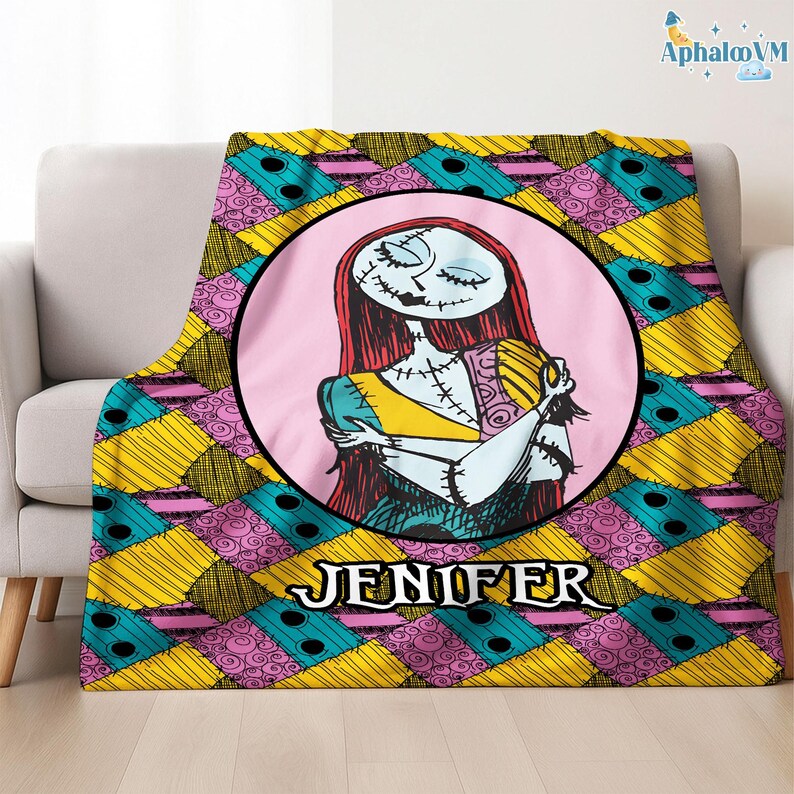 May include: A throw blanket with a circular image of Sally from The Nightmare Before Christmas, with red hair and stitched features, set against a pink background. The blanket has a patchwork design in yellow, teal, and pink, with the name "JENIFER" in white.