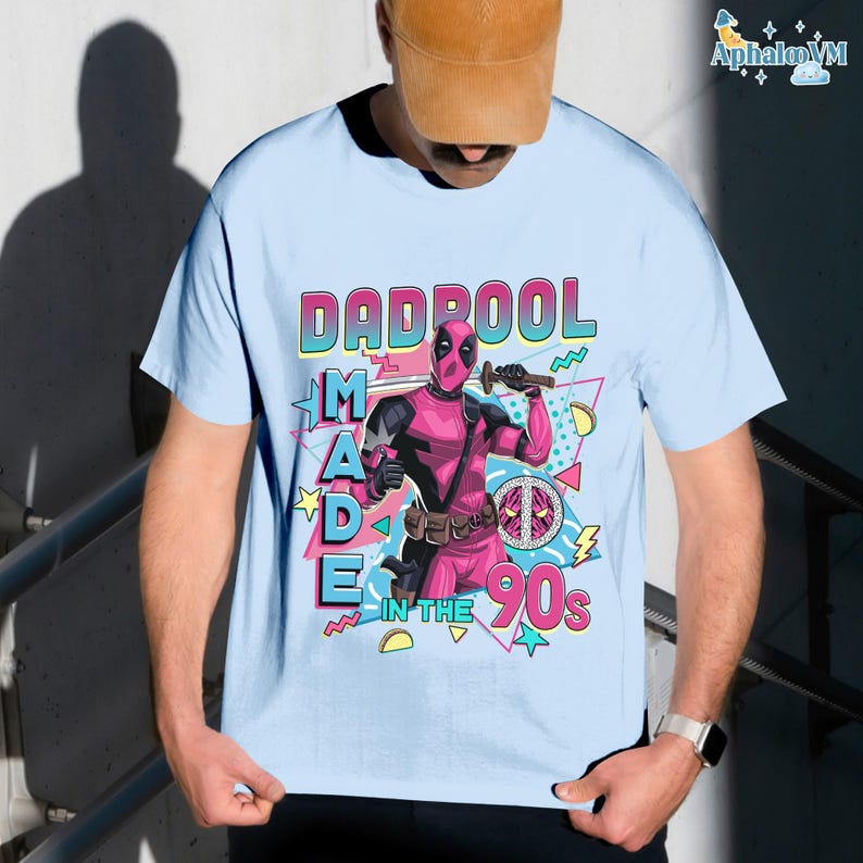 A person wearing a t-shirt with a graphic design featuring a character from the Marvel Cinematic Universe, specifically the character Deadpool. The design includes the text "DAD BOOL MADE IN THE 90'S" and a peace sign.