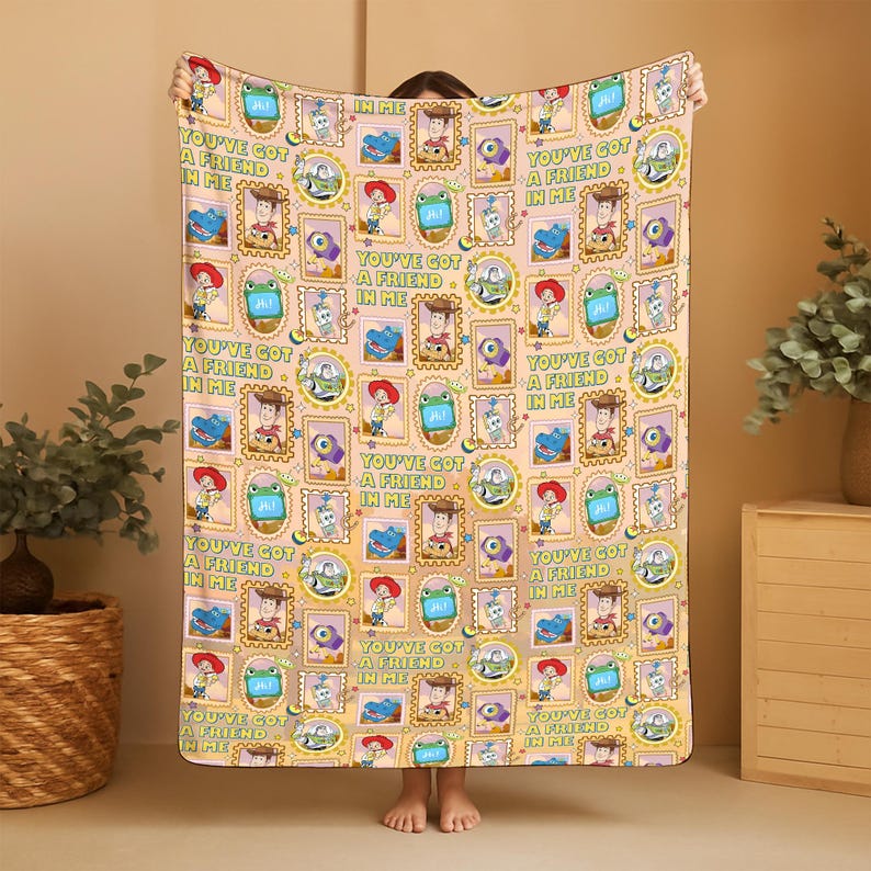 May include: A rectangular throw blanket with a light peach background featuring a repeating pattern of Toy Story characters in frames, including Woody, Buzz Lightyear, and Rex, alongside the text You've Got A Friend In Me in green lettering.