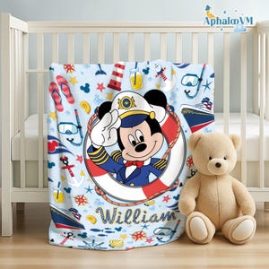 Op de afbeelding: Een lichtblauwe babydeken met een nautisch thema, met Mickey Mouse in een kapiteunsuniform. De deken heeft een patroon van ankers, schepen en nautische elementen. De naam "William" staat op de deken.