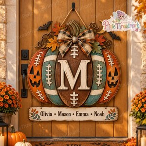May include: A decorative door hanger shaped like a football-themed pumpkin with a large letter M in the center, a plaid bow, and a hanging sign featuring the names Olivia, Mason, Emma, and Noah, accented with autumn leaves and black bats.