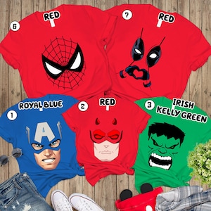 May include: Five short-sleeved t-shirts featuring superhero graphics. Two red shirts display Spider-Man and Deadpool masks. A royal blue shirt shows Captain America, a red shirt features Daredevil, and an Irish Kelly green shirt displays the Hulk.