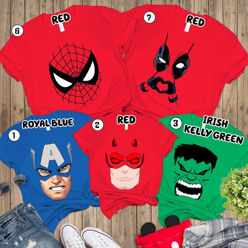 May include: Five short-sleeved t-shirts featuring superhero graphics. Two red shirts display Spider-Man and Deadpool masks. A royal blue shirt shows Captain America, a red shirt features Daredevil, and an Irish Kelly green shirt displays the Hulk.