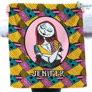 May include: A blanket with a cartoon illustration of a character with red hair, stitched features, and a patchwork dress, set against a pink oval. The blanket has a patchwork design in yellow, teal, and pink, with the name "JENIFER" at the bottom.