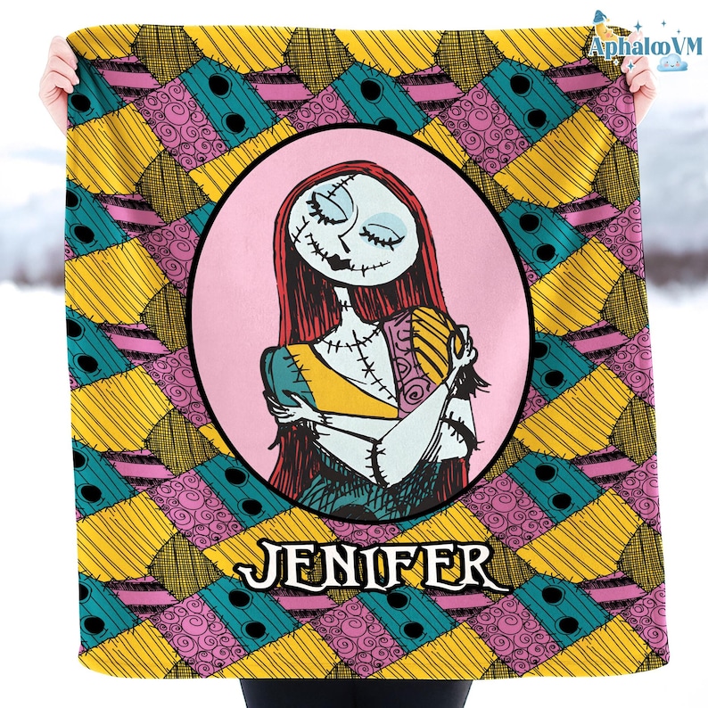 May include: A blanket with a cartoon illustration of a character with red hair, stitched features, and a patchwork dress, set against a pink oval. The blanket has a patchwork design in yellow, teal, and pink, with the name "JENIFER" at the bottom.