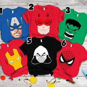 May include: Six short-sleeved t-shirts featuring superhero graphics. Shirt 1 is blue with Captain America, 2 is red with Daredevil, 3 is green with Hulk, 4 is red with Iron Man, 5 is black with Moon Knight, and 6 is red with Spider-Man.