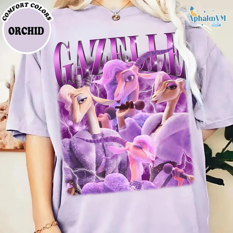A person wearing a purple t-shirt with a graphic design featuring purple and pink cartoon-like characters, including a unicorn and a bird, along with the text "Gazelle" and "Orchid".