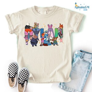 A white t-shirt with a colorful graphic design featuring cartoon characters and the name "Dylan" written in a playful font.