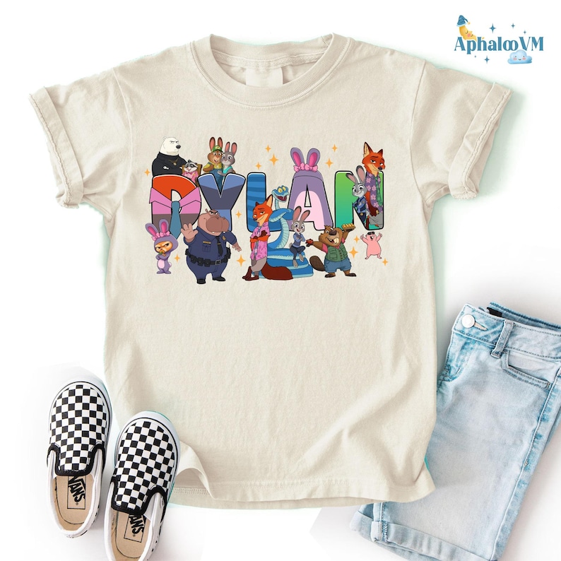 A white t-shirt with a colorful graphic design featuring cartoon characters and the name "Dylan" written in a playful font.