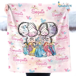 Puede incluir: Una manta rosa con un gran dise&ntilde;o de lazo, un castillo e ilustraciones de princesas. La manta tiene el texto "Sophia Princess" repetido, junto con corazones y formas de cabeza de Mickey Mouse.